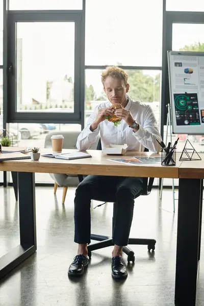Un hombre de negocios pelirrojo con una camisa blanca se centra en el almuerzo mientras participa en un proyecto de trabajo en una oficina elegante. — Stock Photo