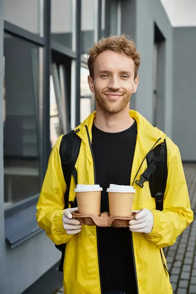A cheerful delivery person holds two cups of coffee outside an office building, ready to brighten everyone's day. — Stock Photo