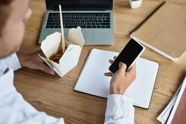 A businessman in a white shirt multitasks by reviewing a project and enjoying noodles in a modern workspace. — Stock Photo