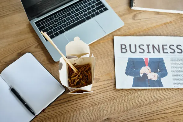 Asian noodles with chopsticks near laptop and business newspaper — Stock Photo