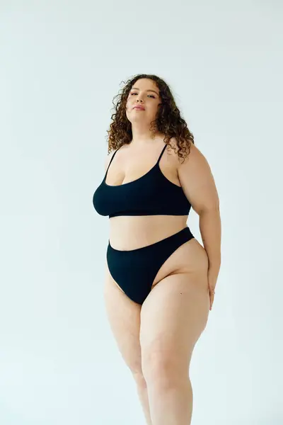 A confident plus size woman flaunts her beauty in elegant black swimwear against a bright backdrop. — Stock Photo