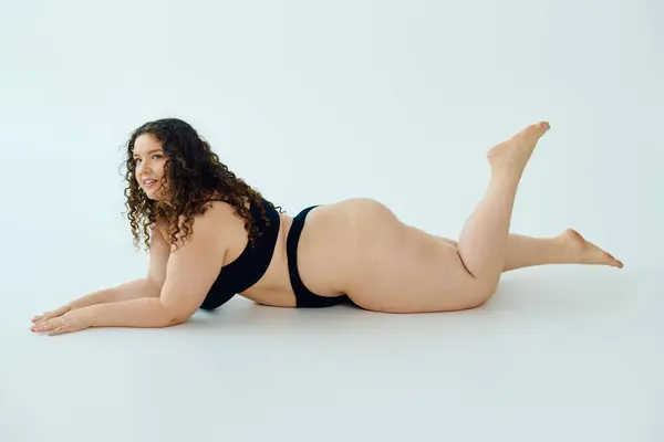 A plus size woman exudes confidence as she poses on her stomach, showcasing her beauty and curves. — Stock Photo