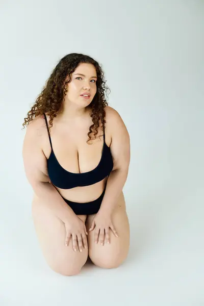 A radiant plus size woman showcases her confidence while kneeling on a smooth surface. — Stock Photo