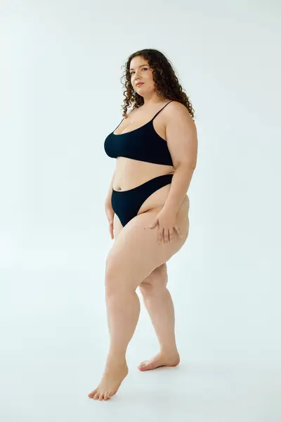 A confident plus size woman poses gracefully against a minimalist backdrop, celebrating her beauty. — Stock Photo