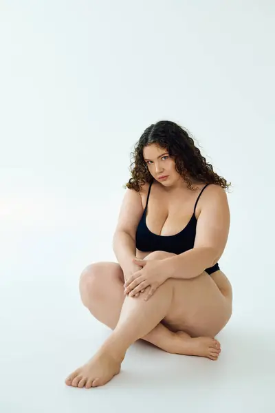 Una donna fiduciosa plus size siede pensieroso, irradiando bellezza su uno sfondo semplice. — Foto stock