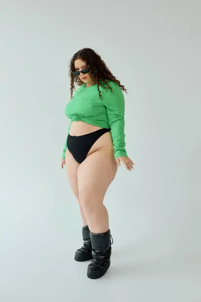 Una mujer segura de tamaño más muestra su top verde chic y botas con estilo. - foto de stock