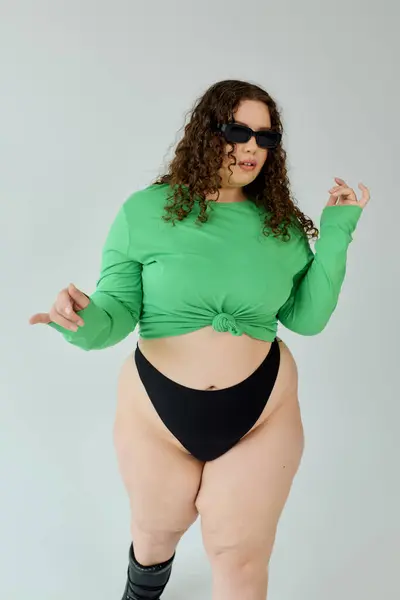 Красивая женщина plus size уверенно позирует в стильном зеленом топе и солнцезащитных очках. — стоковое фото