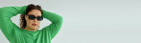 Una impresionante mujer de talla grande muestra su estilo en una vibrante parte superior verde y gafas de sol elegantes. - foto de stock