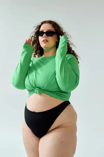 Женщина plus size уверенно демонстрирует свой уникальный стиль в ярком зеленом топе и черном нижнем белье. — стоковое фото