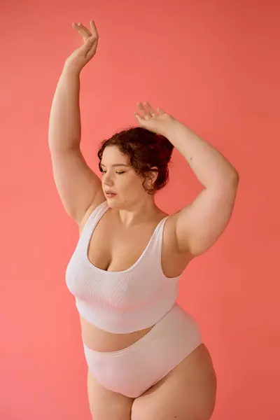 A plus size woman poses confidently, embracing her beauty in a stunning pink backdrop. — Stock Photo