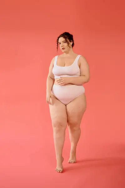 A confident plus size woman showcases her beauty in a pastel pink outfit, posing with grace. — Stock Photo