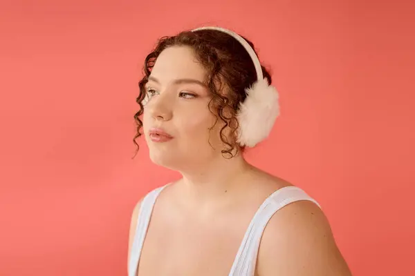 A joyful plus size woman with curly hair showcases stylish earmuffs while gazing thoughtfully. — Stock Photo