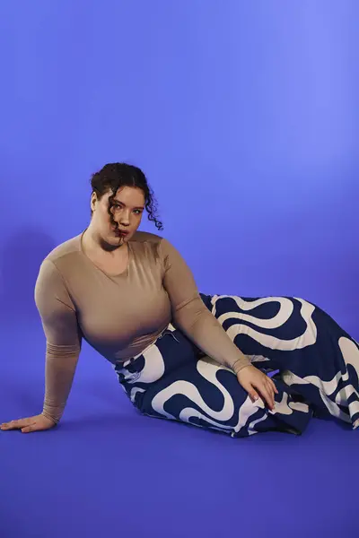 A confident plus size woman lounges in fashionable attire with a bright blue background. — Stock Photo