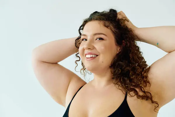 Eine strahlende Plus-Size-Frau mit lockigem Haar lächelt freundlich, während sie spielerisch mit ihren Händen posiert. — Stockfoto