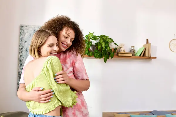 Dos mujeres jóvenes comparten un cálido abrazo, riéndose juntas en un espacio vibrante y elegante. - foto de stock