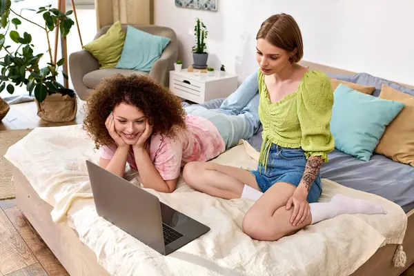 A lovely couple relaxes on a bed, sharing smiles while watching something amusing on a laptop. — Stock Photo