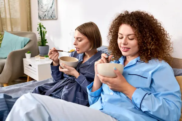 Deux jeunes femmes partagent un repas joyeux dans leur chambre confortable, s'embrassant compagnie. — Photo de stock
