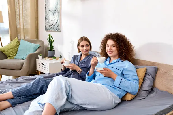 A beautiful young couple relaxes at home, sharing laughter and warm drinks in comfortable attire. — Stock Photo