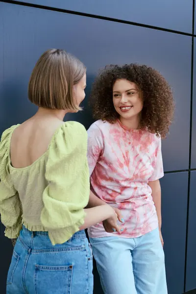 Dos mujeres jóvenes disfrutan de su tiempo juntas, riendo y tomándose de la mano en un telón de fondo moderno. — Stock Photo