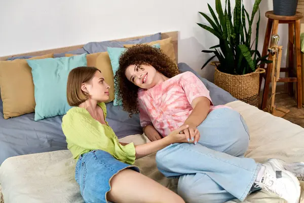 Deux jeunes femmes partagent un moment tendre tout en se prélassant sur un lit confortable entouré de verdure. — Photo de stock