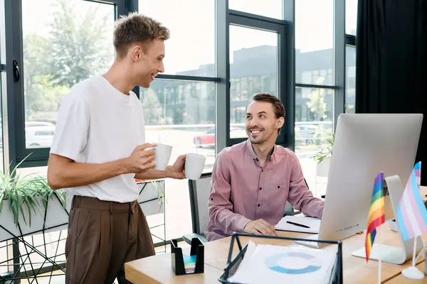 A stylish gay couple enjoys a light hearted conversation over coffee in a modern office setting. — Stock Photo