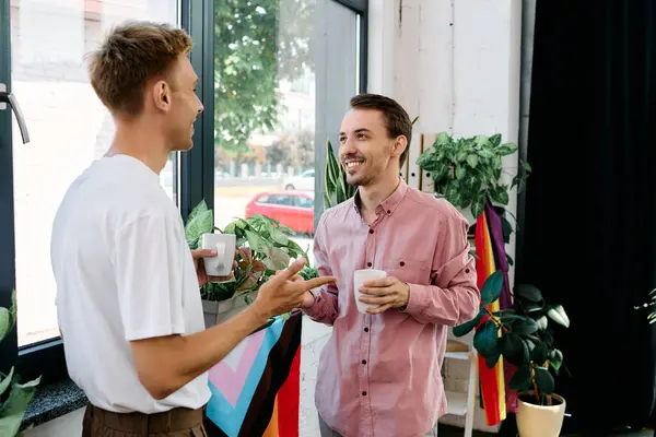Dos encantadores individuos comparten risas y bebidas en un ambiente acogedor y lleno de plantas. - foto de stock