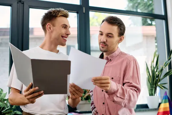 Dos hombres disfrutan de un momento alegre discutiendo los papeles en un interior soleado, elegante y verde. - foto de stock
