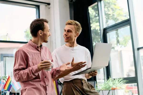 Two men share laughter and ideas over a laptop in a vibrant, sunlit workspace. — Stock Photo