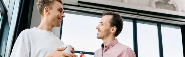 Two charming men enjoy a heartfelt conversation, sipping drinks in a warm, inviting office. — Stock Photo