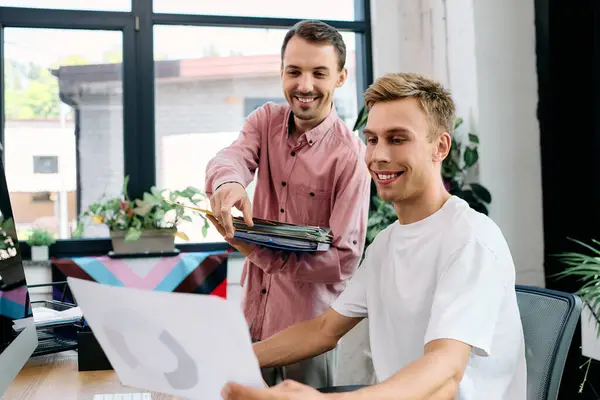 Two happy men share a lighthearted discussion while reviewing creative work together. — Stock Photo