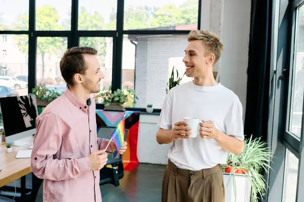 Two stylish men share a warm conversation while holding cups in a bright room filled with greenery. — Stock Photo