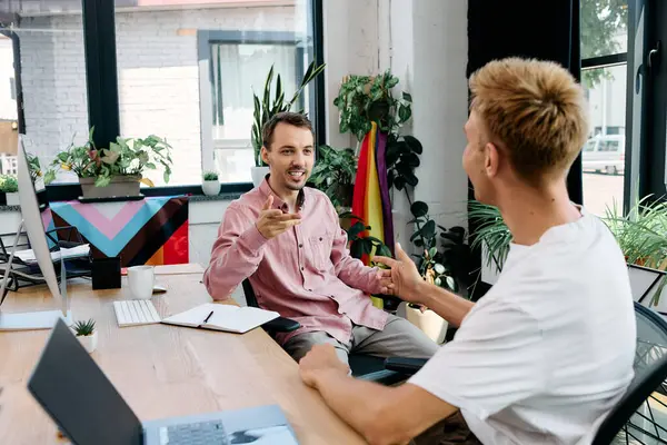 Two stylish men share a joyful discussion in a bright and inviting office space. — Stock Photo