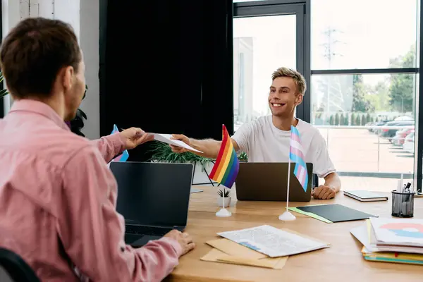 Due uomini attraenti si impegnano in uno scambio amichevole mentre lavorano alle loro scrivanie, irradiando positività.. — Foto stock