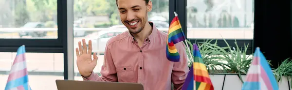 Joyful man working in office surrounded by colorful pride flags. — Stock Photo
