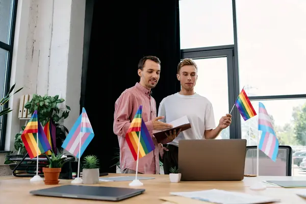 Two men engaged in a lively discussion, surrounded by pride flags in a bright office. — Stock Photo