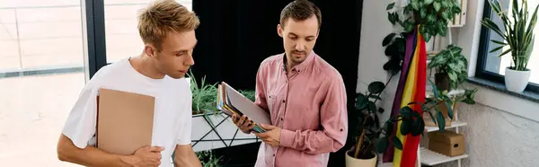 Two trendy men exchange ideas while surrounded by greenery and vibrant decor in their workspace. — Stock Photo