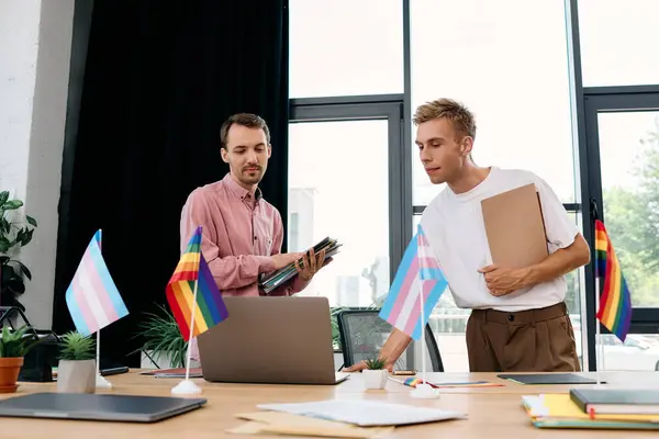 Two handsome men engage in a creative discussion at a colorful, pride themed office. — Stock Photo