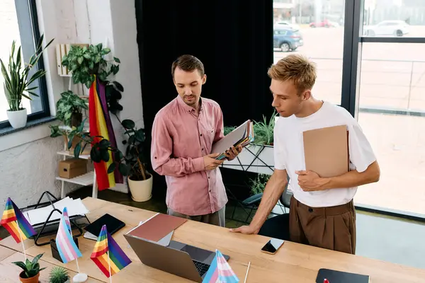 Two stylish men discuss creatively at a modern desk adorned with pride decorations. — Stock Photo