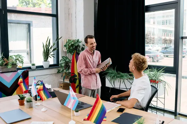 Dois homens elegantes trocam sorrisos enquanto discutem projetos criativos em um ambiente vibrante. — Fotografia de Stock