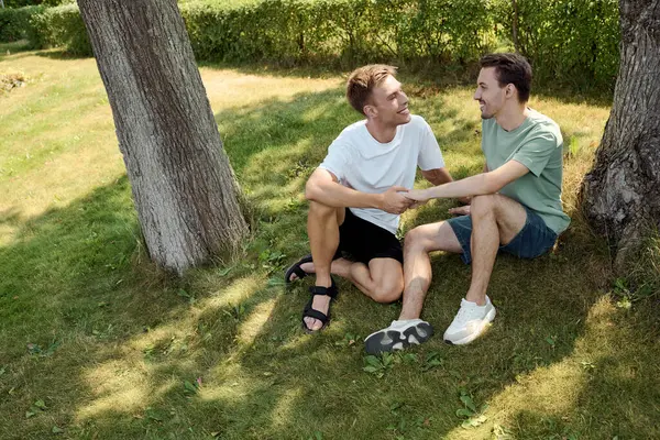 Two smiling men share a tender moment on a sunny afternoon, surrounded by greenery. — Stock Photo