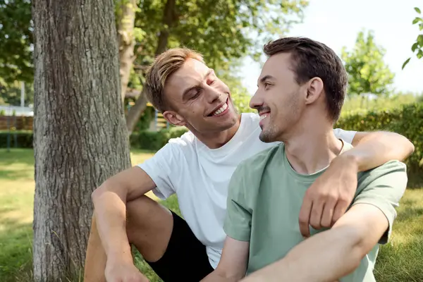 Two charming men share a loving gaze in a sunny park, enjoying each others company. — Stock Photo