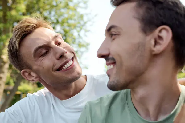 Two charming men share smiles and laughter while embracing in a vibrant park setting. — Stock Photo
