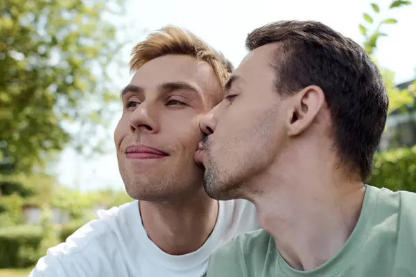 A joyful couple shares a loving kiss while enjoying a warm afternoon in a vibrant park. — Stock Photo