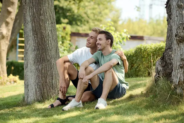 A handsome gay couple relaxes on the grass, sharing laughter and enjoying each others company. — Stock Photo