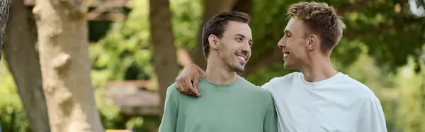 Deux hommes souriants profitent d'un après-midi ensoleillé dans un beau parc, embrassant leur amour les uns pour les autres. — Photo de stock