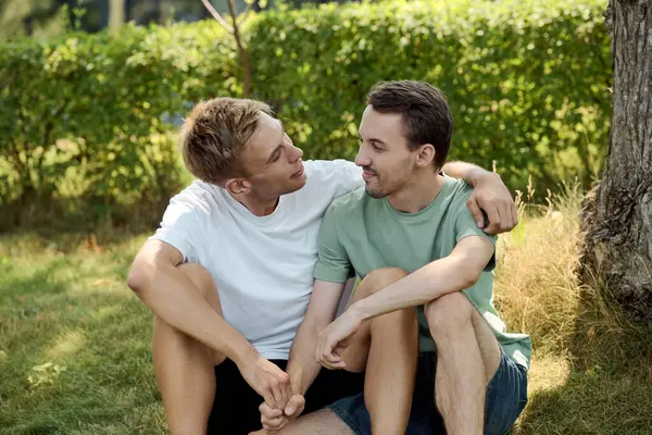 Two men sit close together in a garden, sharing laughter and affectionate glances under the sun. — Stock Photo