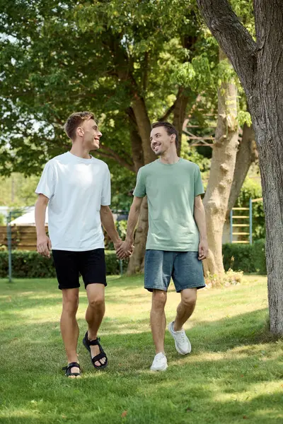 A joyful couple strolls hand in hand through a green park, sharing smiles and laughter. — Stock Photo