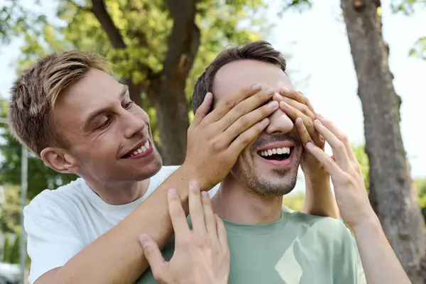 Two smiling men share a playful moment outdoors, surrounded by greenery and sunshine. — Stock Photo