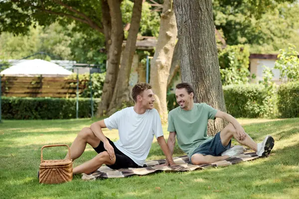 Two smiling men enjoy a cozy picnic on a sunny day surrounded by natures beauty. — Stock Photo