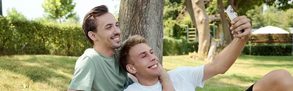 Zwei lächelnde Partner fangen eine freudige Erinnerung ein, während sie sich an einem sonnigen Tag in einem lebendigen Park entspannen. — Stockfoto